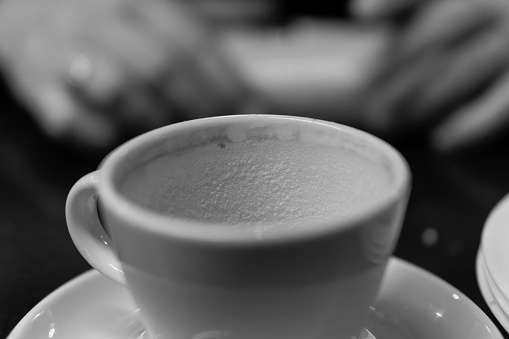Empty frothy coffee cup, with a woman's hands behind it.