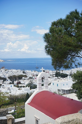 Portrait shot of a small Greek Orthodox Church on a hill, overlooking the sprawling Old Town of Mykonos, Greece