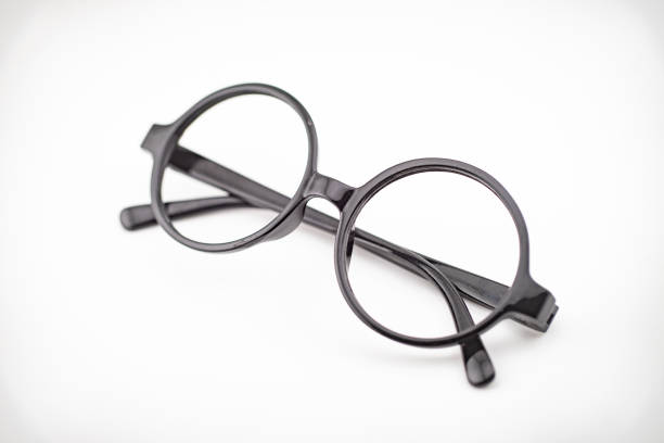 Close-up of vintage round eyeglasses with thin brown frames resting on a reflective surface, with soft bokeh lights glowing in the blurred background.