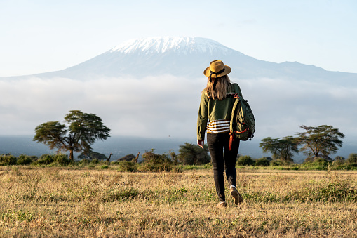 A young beautiful girl walks through the savannah against the backdrop of Mount Kilimanjaro during a walking safari, travel concept, peaceful relaxing moment. happy earth day