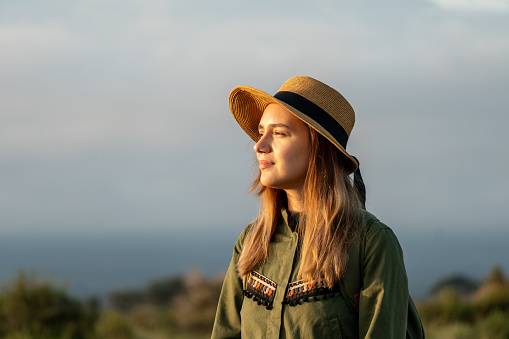 A beautiful young girl In a hat stands against the backdrop of the Kilimanjaro volcano and looks away. The concept of tourism and African safari.