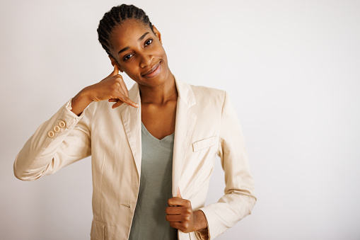 Portrait of beautiful young black woman on white background showing phone gesture with hand and fingers. Communication concepts.