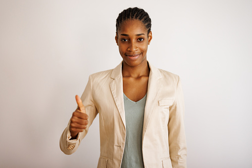 Portrait of beautiful young black woman on white background giving a thumb up gesture of approval and success