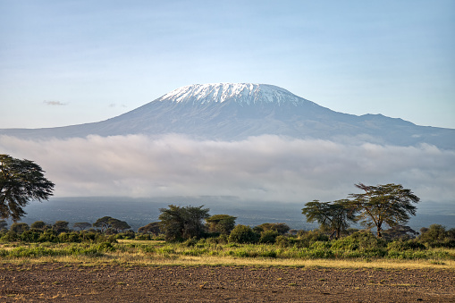 Kilimanjaro mountain Tanzania snow capped under cloudy blue skies captured whist on safari in Africa Kenya. Beautiful African landscape with mountains and savannah