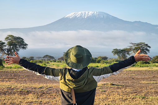 man walks against backdrop of Kilimanjaro. African walking safari. male traveler with backpack looking at amazing mountains. Hands to the side. travel concept, atmospheric epic moment