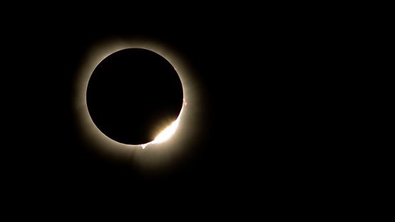 Beautiful solar eclipse photo of the sun almost totally eclipsed by the moon against a black sky background. Diamond ring effect and red solar filaments can be seen. Copy space