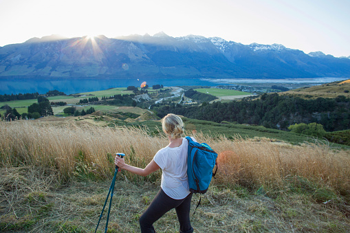 Hiker looks across agricultural fields towards sun setting over distant mountains