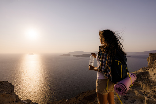 Young female hiker having water break on a hill above the sea and looking at view. Copy space.