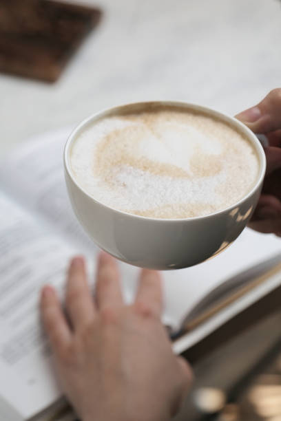 istock Person Holding Coffee Cup Over Open Book 2148099381