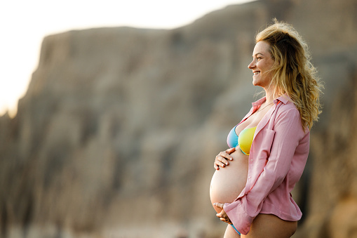 Happy expecting woman day dreaming during summer day on the beach. Copy space.