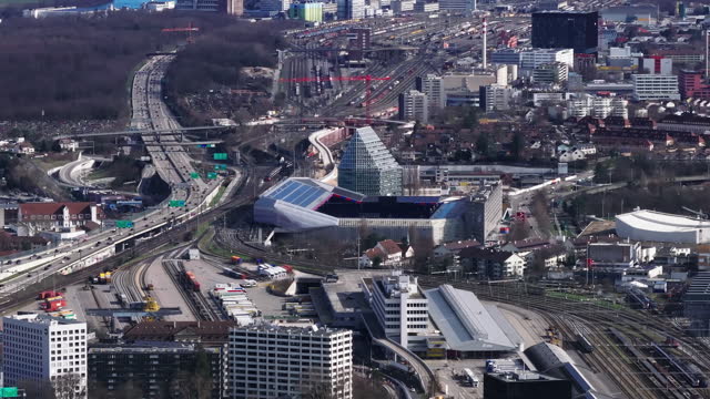 Aerial view of modern football stadium and busy multilane highway leading around. Large railroad yard in background. Basel, Switzerland