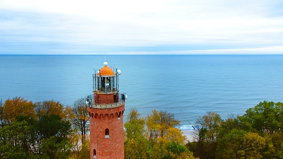 Drone-captured image of Gski Lighthouse, Poland, on a cloudy November day. The serene sea, gentle waves, and empty beach create a tranquil coastal scene, offering a peaceful retreat by the Baltic.