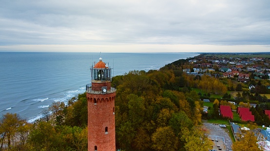 Drone-captured image of Gski Lighthouse, Poland, on a cloudy November day. The serene sea, gentle waves, and empty beach create a tranquil coastal scene, offering a peaceful retreat by the Baltic.