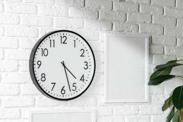 minimalist white wall decor featuring a clock and blank photo frames - customisable fotografías e imágenes de stock