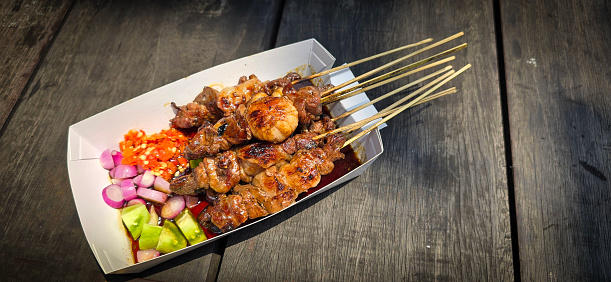Lamb grilled satay served with barbecue savory sauce and pickled onion, chili and cucumber, selective focus photo on top of wooden table