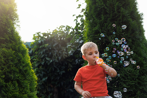 Park, child and boy blowing bubbles enjoying fun time alone outdoors, joy and childhood development. Happy, freedom and kid learning and playing with soap bubble toy or wand and relax on grass