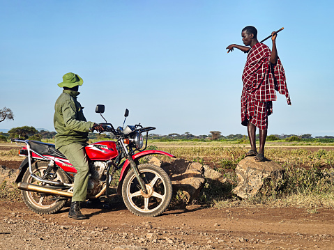February 5, 2024. amboseli Kenya.: the maasai man from the Masai tribe in the red national clothes communicates with a pager on a motorcycle in the African savannah.