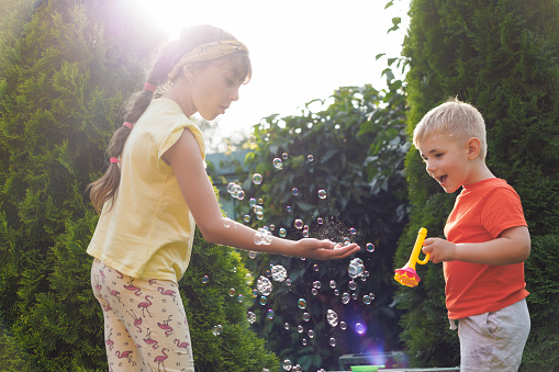 Playing, garden and children blowing bubbles for entertainment, weekend and fun activity together. Recreation, outdoors and siblings with a bubble toy for leisure, childhood and enjoyment in summer