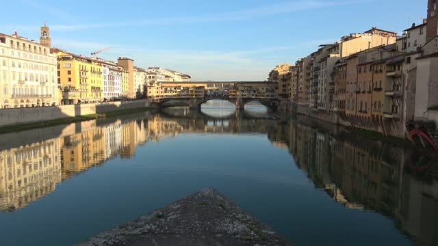 The Ponte Vecchio, old segmental arch bridge with stores and housing over the Arno River, in Florence, Italy. Golden reflections on water