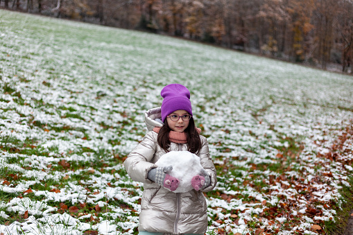 Cute little girl making snowman in the park on cold winter day