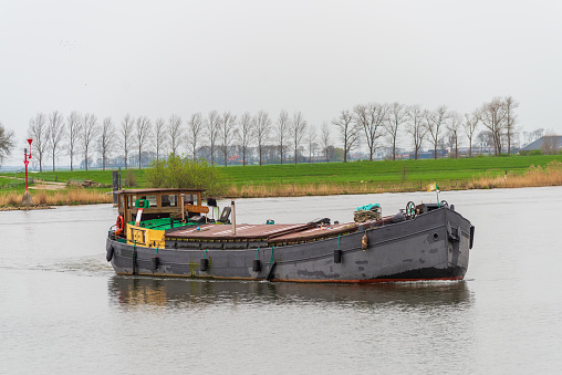 Kampen, Netherlands - March 30, 2024: Small cargo ship on the IJssel river, entering the Haatland harbor in Kampen