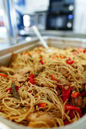 A selection of meal options is displayed at a catered buffet featuring a pan of noodles with vegetables and a dish with a red sauce, ready for guests to serve themselves during a midday gathering.