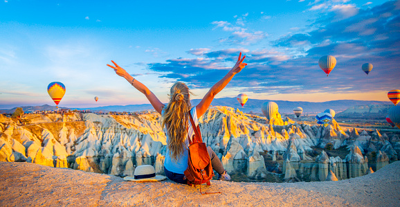 Happy woman enjoying panoramic view of Cappadocia landscape and colorful hot air balloons in the sky- Travel destination concept Turkey