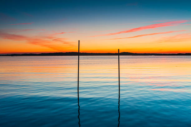 Poles standing in sea at colorful sunset