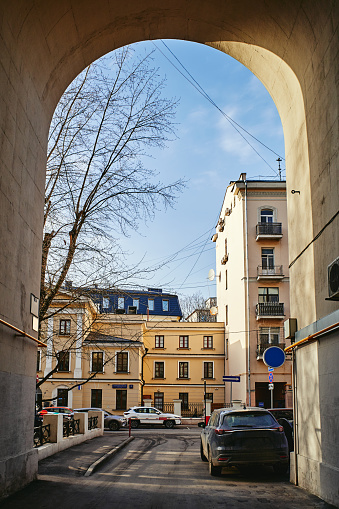 Passage arch in a house onto a street with parked cars and buildings, clear blue sky