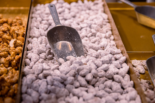 Sugared almonds. Candied sugar coated caramelized  almond nuts sold on the counter at the Christmas fair market. Pile of roasted sweets on the metal tray with serving spoon. Close up Selective focus.