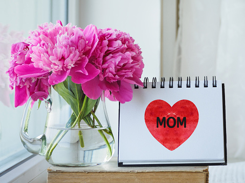 Notepad with the word MOM and a drawn red heart. Preparation for the holidays. Close-up, indoors. Congratulations for family, loved ones, relatives, friends and colleagues