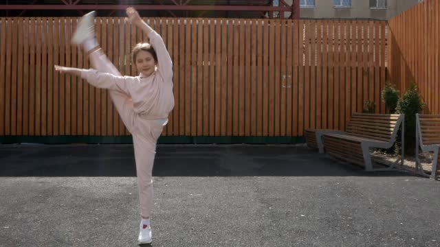 A girl in sportswear demonstrates an element of gymnastics. Gymnast doing sports on a city street. The concept of plasticity, balance, sports lifestyle among teenagers and children