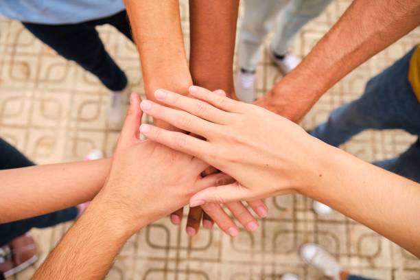 Group of young adults putting hands together symbolizing teamwork and cooperation in a business setting
