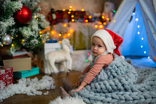 Cute little girl whit blanket sitting next to Christmas tree