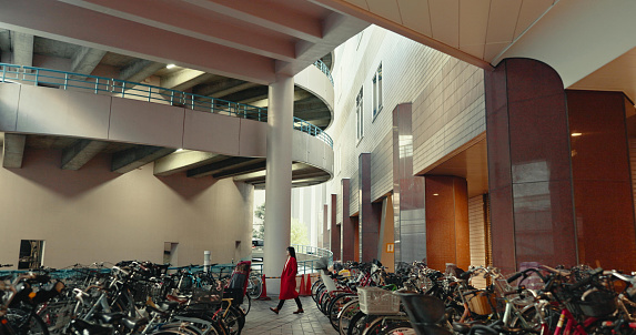 City, walking and woman in building with bicycle for travelling, commute and bike parking or station. Transport, urban town and Japanese person with storage for sustainable vehicles for journey