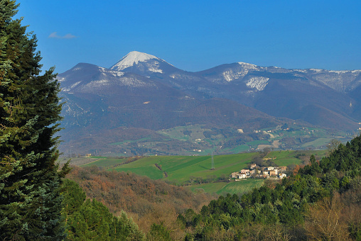 Landscape in rural Marche region, central Italy. San Vicino snowy peak over Argignano village, Fabriano.