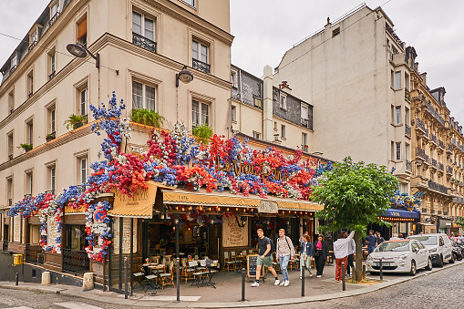 Paris, France - July 13, 2023: Pedestrians in front of a street cafe decorated with flowers in the Montmartre district.