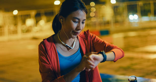 istock Young Asian female athlete runner checking progress on smart watch and looking at smart watch heart rate monitor before running exercise outdoors at night in urban. Healthy workout exercise. 2148115798