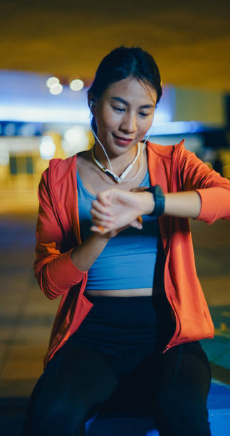 istock Young Asian female athlete runner checking progress on smart watch and looking heart rate monitor before running outdoors at night in urban. Healthy workout exercise. Vertical Screen. 2148115801