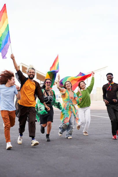 istock People celebrating the pride day, holding rainbow flags while running excited and looking at camera. 2148117058