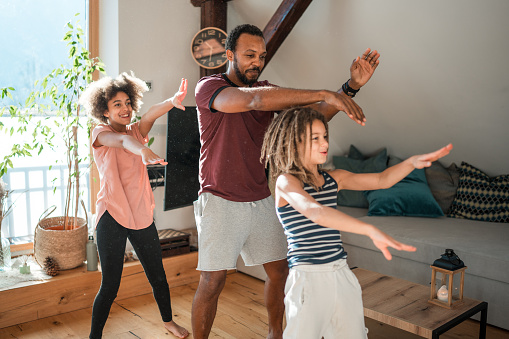 A diverse family with a male and two children joyfully dancing in their living room, expressing happiness and togetherness.