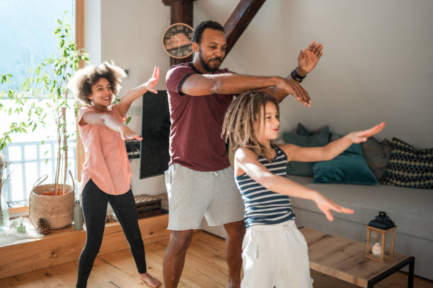 Diverse Family Enjoying Playful Dance Together Indoors A diverse family with a male and two children joyfully dancing in their living room, expressing happiness and togetherness. dancing dad stock pictures, royalty-free photos & images