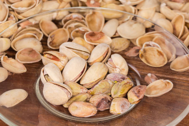 istock Partly peeled pistachio nuts on transparent saucer against empty shells 2148119324