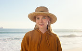 Portrait, waves and happy woman on beach with hat for travel, adventure and tropical holiday in Bali. Relax, water and face of happy girl at ocean with sunshine, weekend vacation and peace on island.