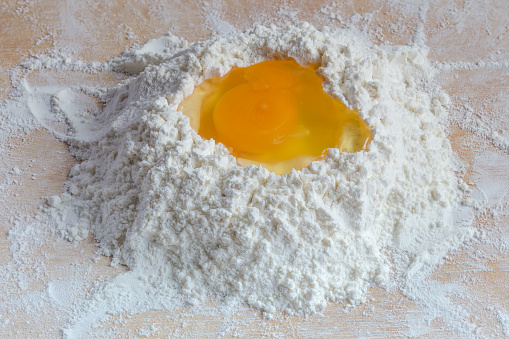 Broken egg in the center of a heap of sifted wheat flour on a wooden board, close-up