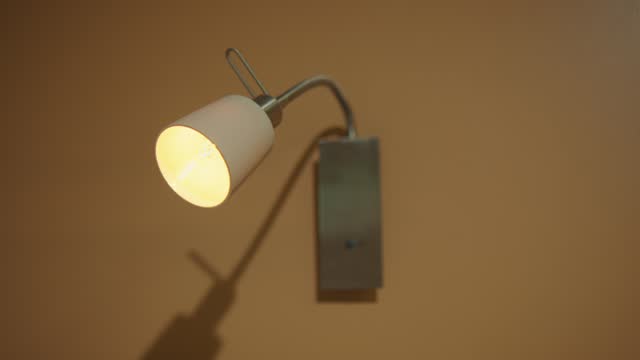 Modern wall-mounted lamp with illuminated bulb against a warm beige background, creating a cozy atmosphere.