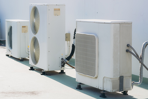 Air conditioner compressor installed on the wall of a building, along with industrial air conditioning units and ventilation systems. Cooling systems.