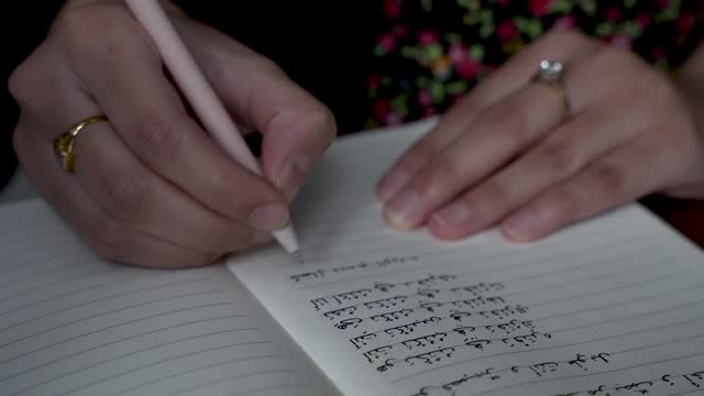 Person practices writing Arabic letters in a notepad, highlighting the concept of learning and mastering letters in a different language. Static Shot