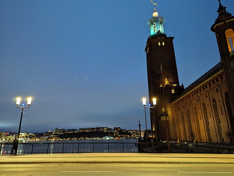 Stockholm City Hall stands tall beside a well-lit street during the blue hour, with city lights starting to illuminate the evening sky
