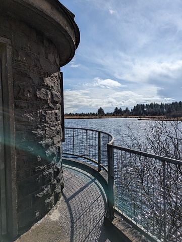 A scenic view from a stone turret with a curved railing, looking out over a tranquil lake and a clear sky